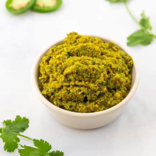 a bowl of green curry paste on a table with sliced chillies.