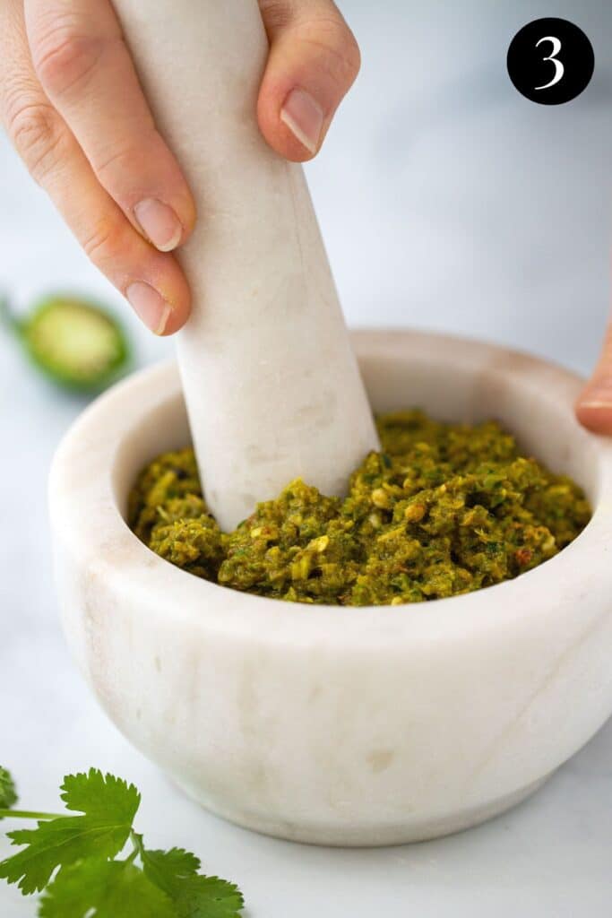 hands using a mortar and pestle to crush curry paste ingredients.
