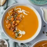 a bowl of soup topped with a swirl of cream and cubed roast pumpkin.