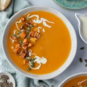 a bowl of soup topped with a swirl of cream and cubed roast pumpkin.