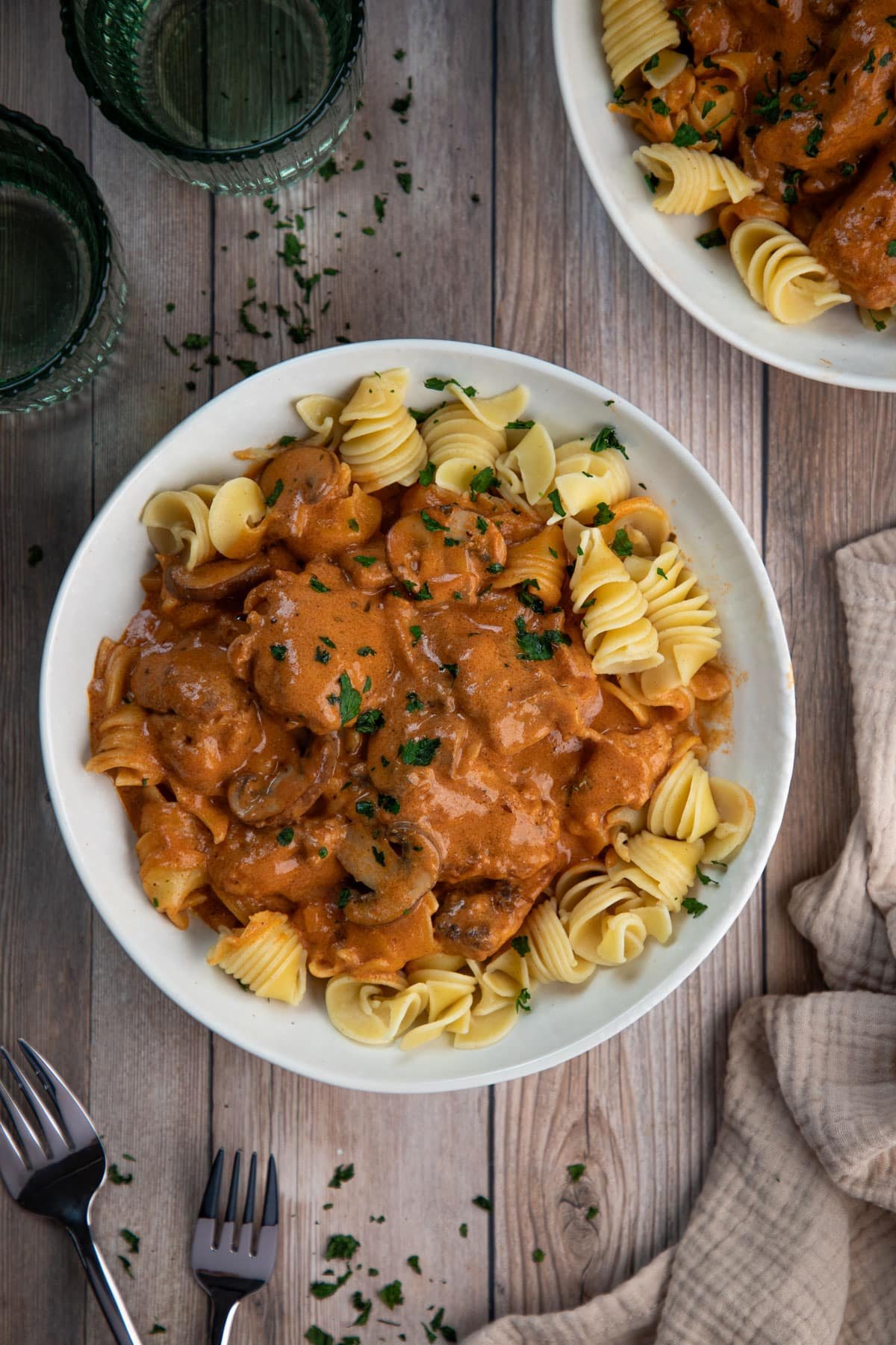 a bowl of pasta topped with chicken stroganoff and herbs, on a table.
