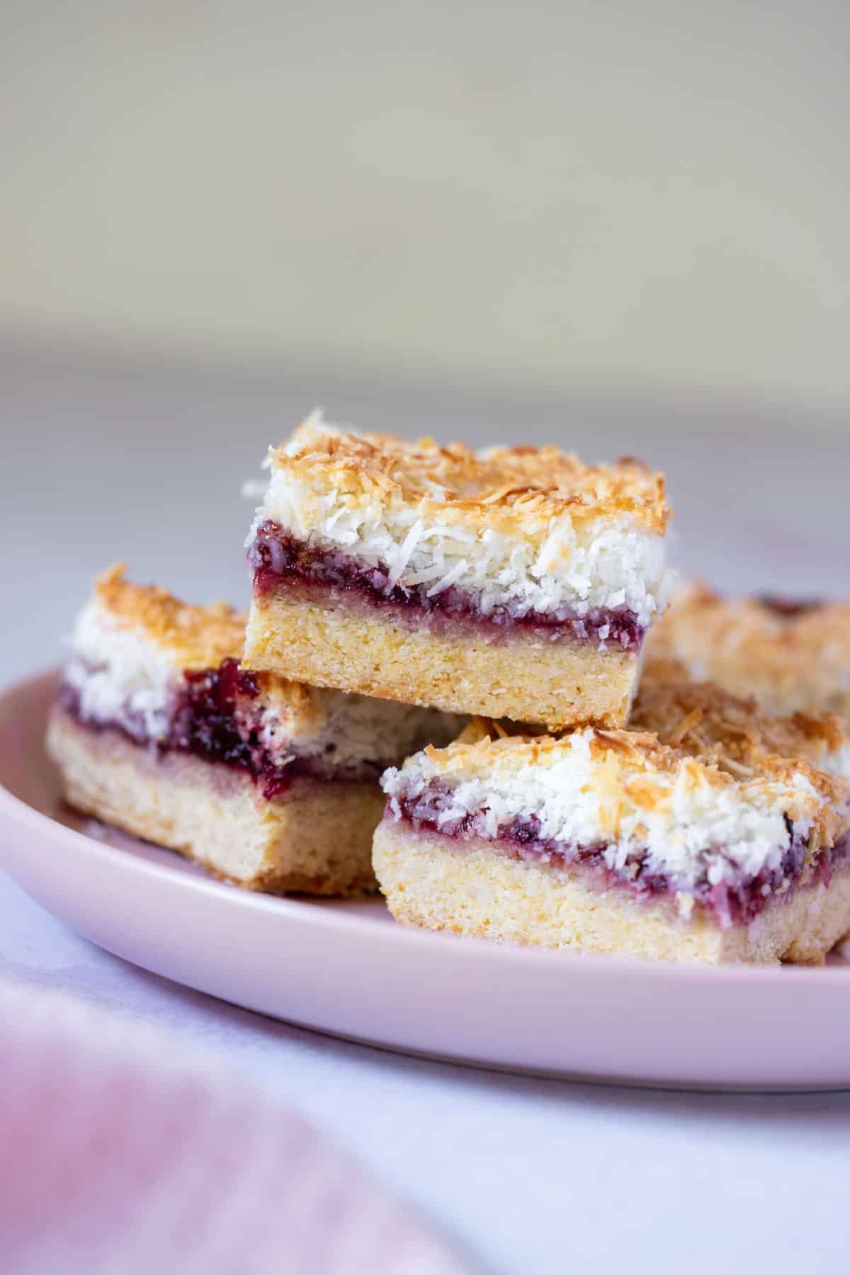 pieces of coconut jam slice, layered on a pink plate.