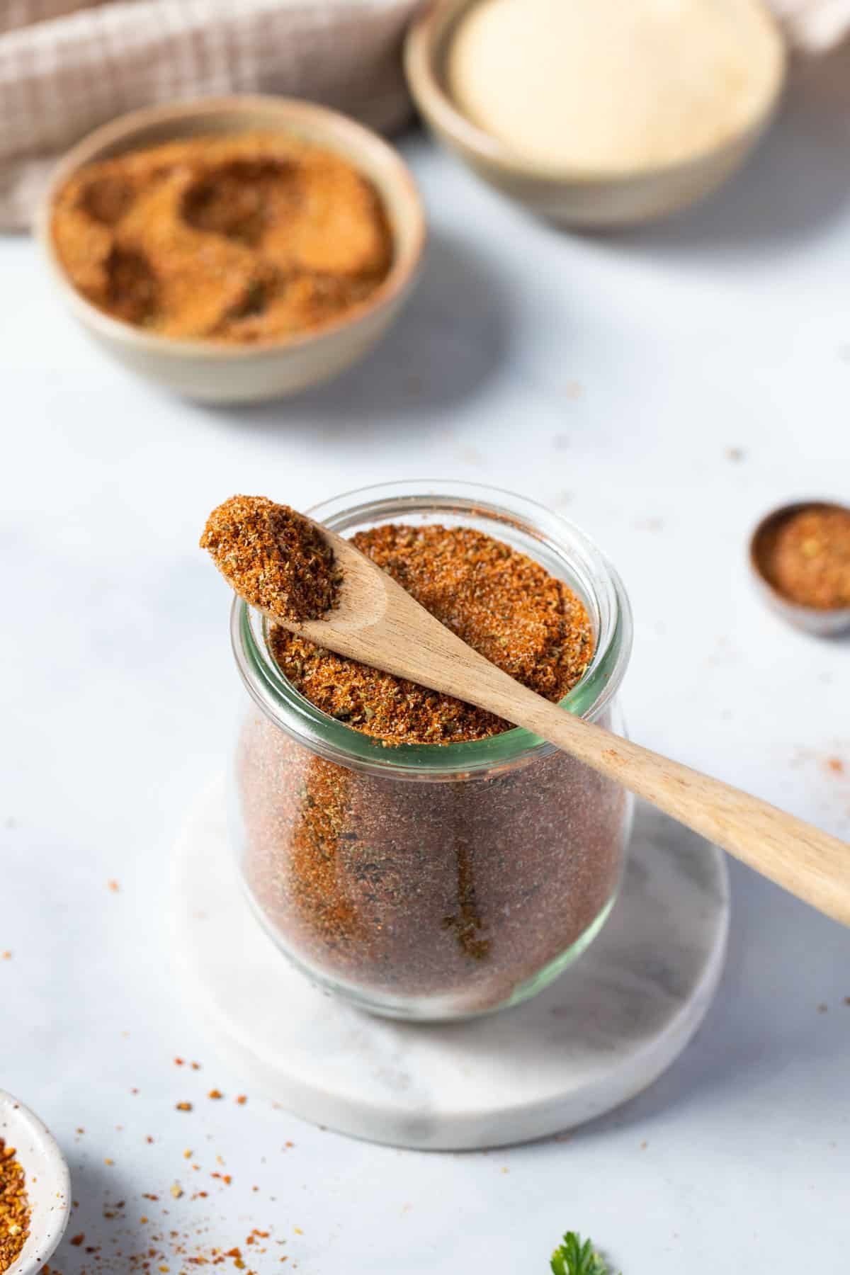 a jar of taco seasoning on a white table with a spoon.