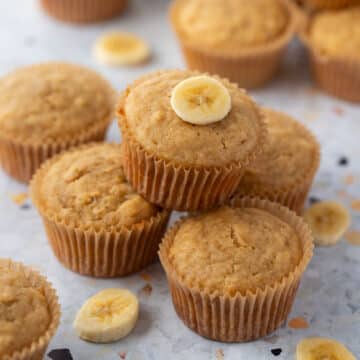 banana muffins arranged on a table, with pieces of sliced bananas.