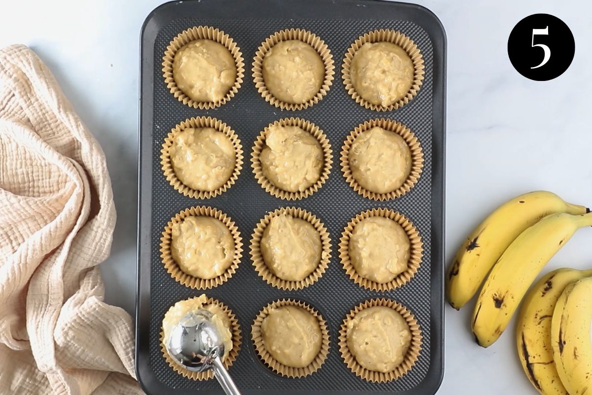 muffin mixture being added to a muffin tin lined with paper cases.