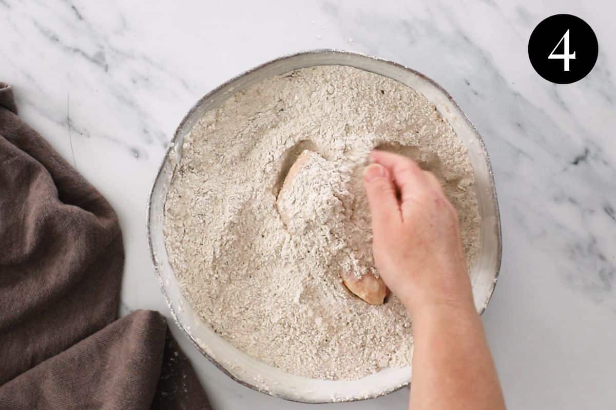 a piece of chicken being coated in flour mixture.