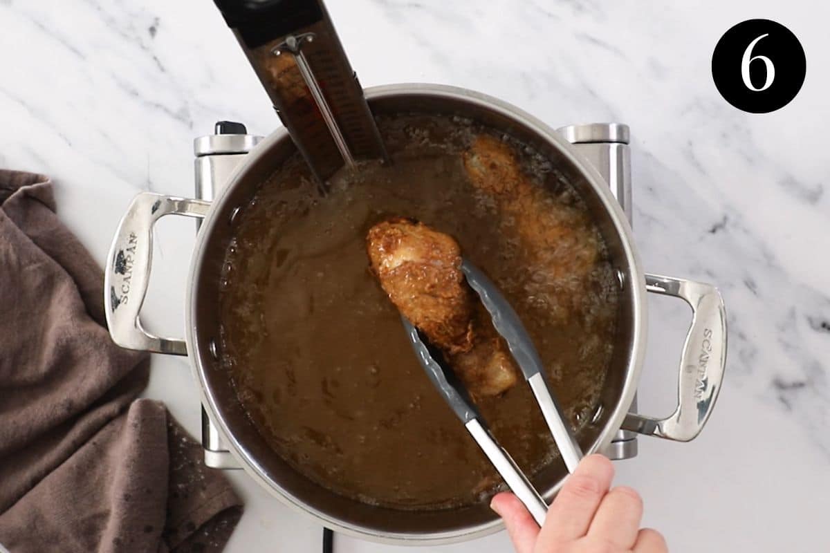 pieces of chicken frying in a pot of oil.