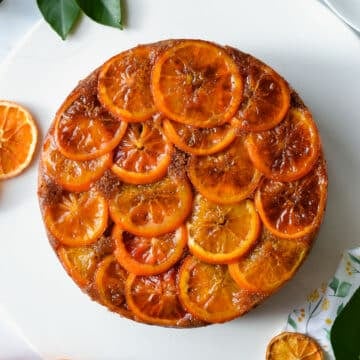 a whole cake, topped with orange slices, on a white plate.