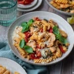 a bowl of pasta with chicken, sun dried tomatoes and basil on a table.