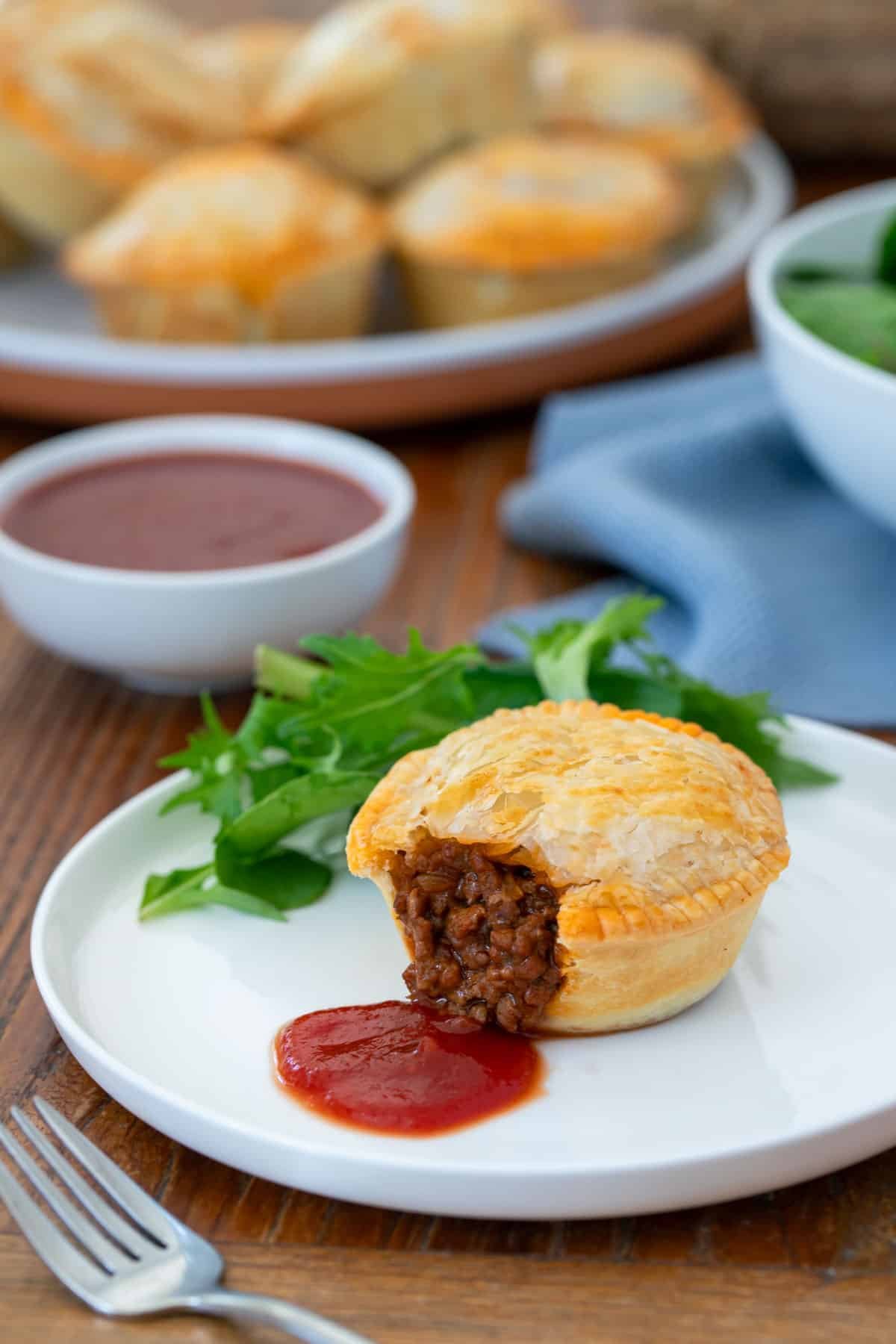 a pie on a plate with tomato sauce. the pie is cut open, showing the beef filling.