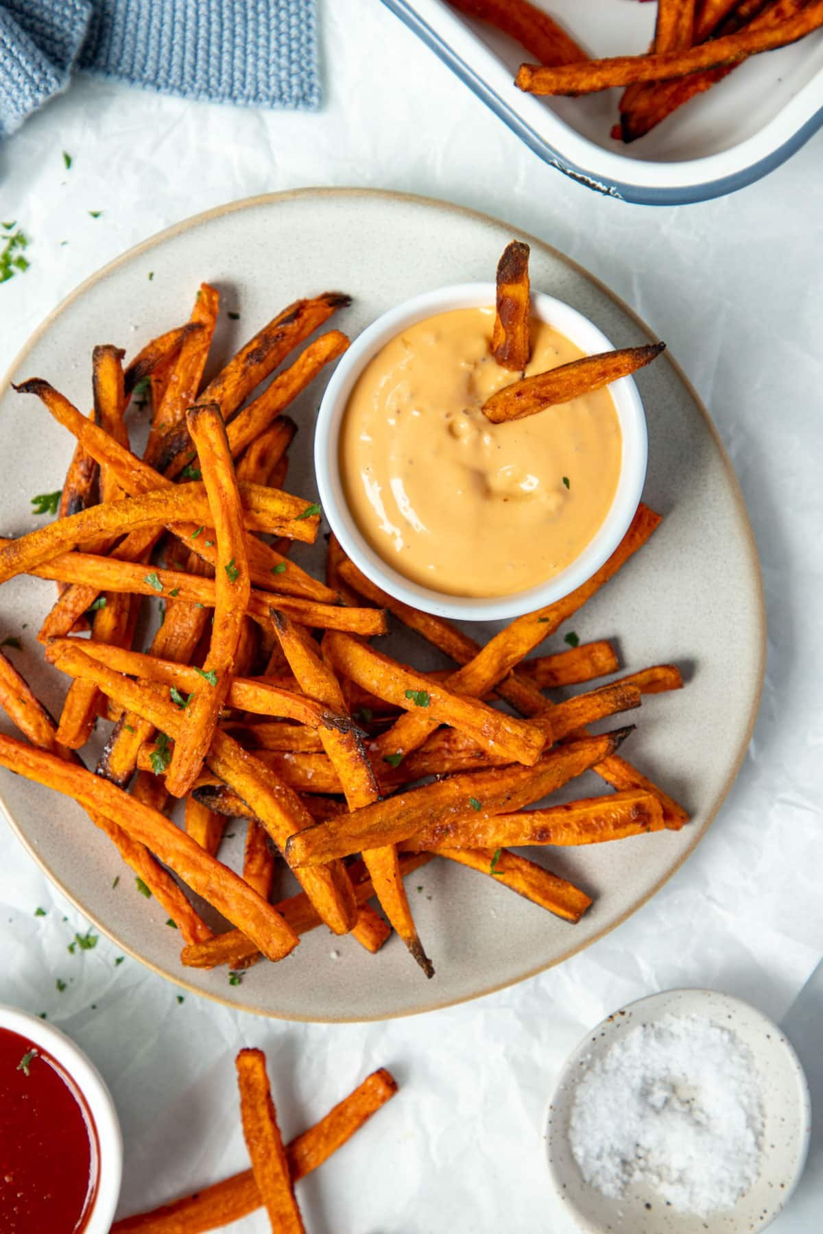 a plate of sweet potato fries on a table with dipping sauces.