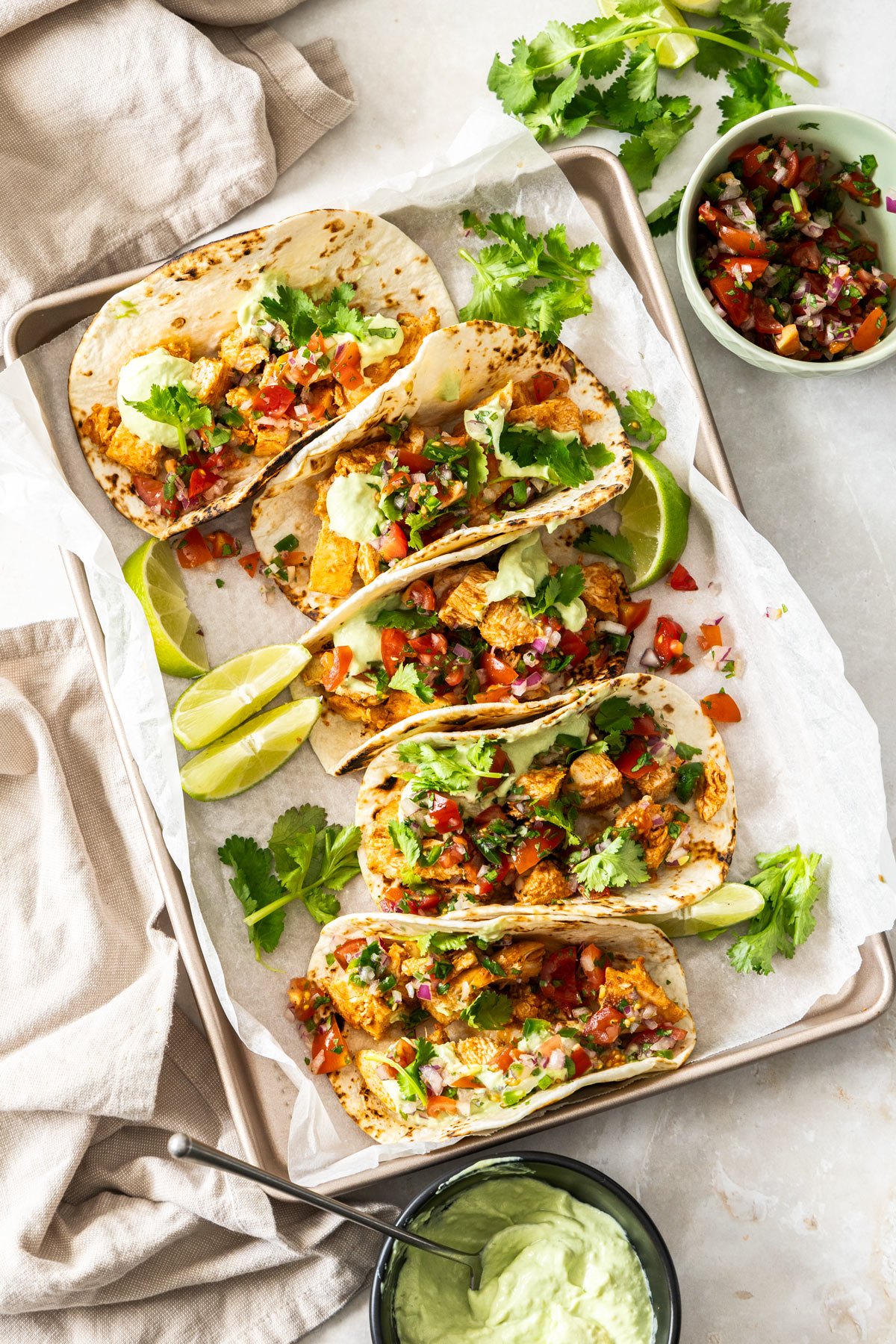 chicken tacos arranged on a metal tray. They are topped with salsa and herbs.