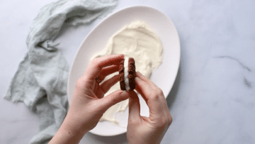 chocolate ripple biscuits being sandwiched together with whipped cream in the middle.