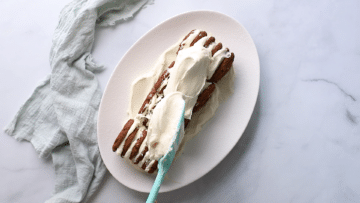 whipped cream being spread over chocolate ripple cake on a plate.