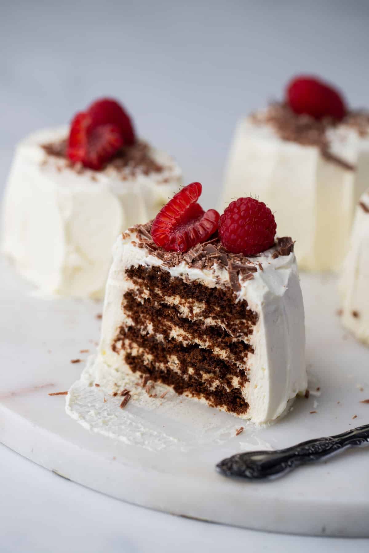 individual chocolate ripple cakes on a plate, topped with raspberries and chocolate.