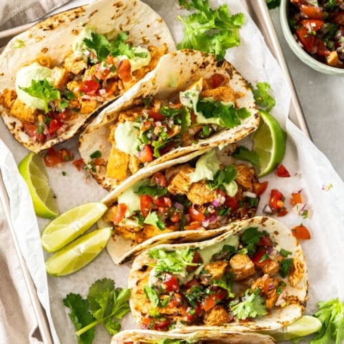 chicken tacos, arranged on a tray with salsa and lime wedges.