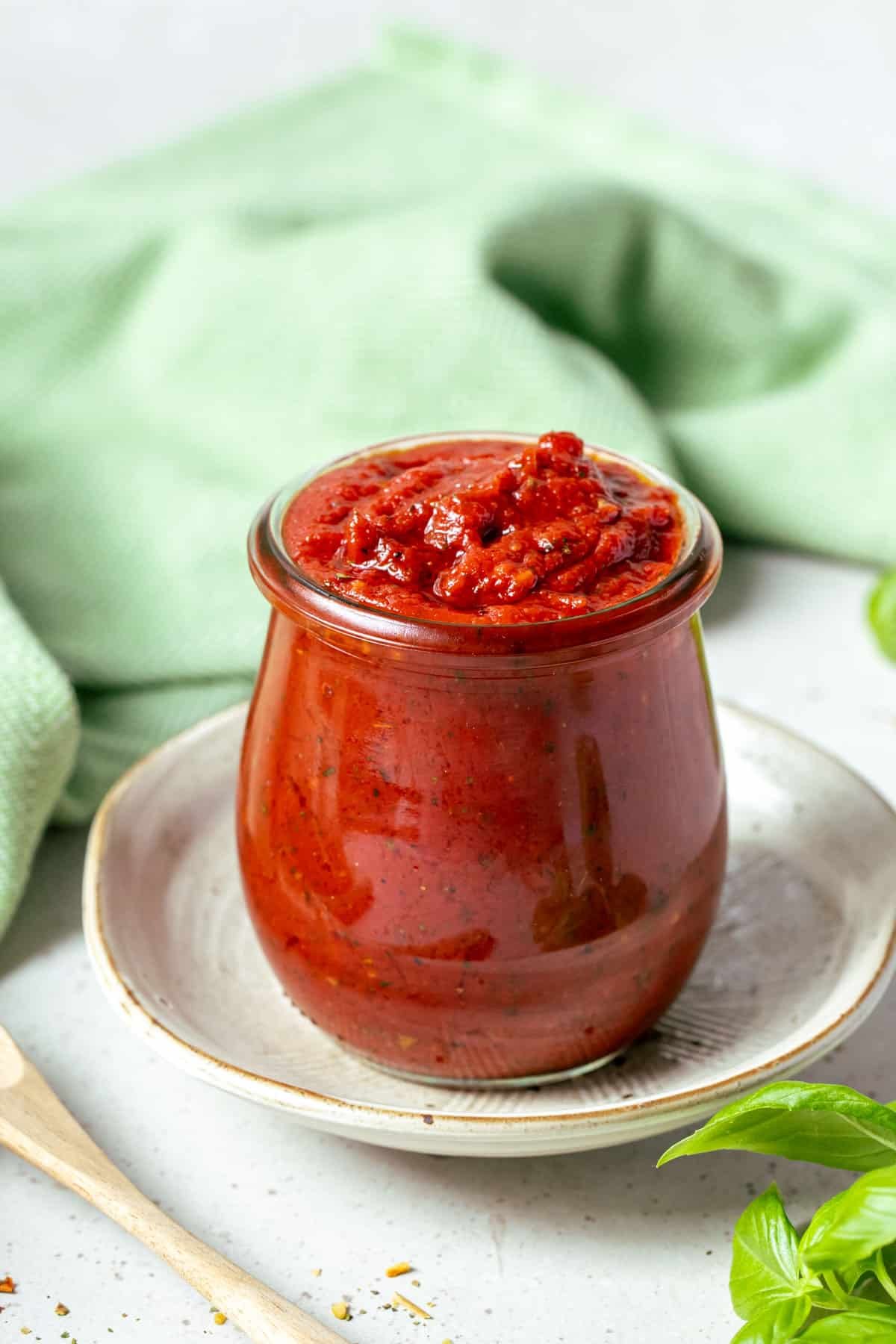 a jar of pizza sauce on a table with basil and herbs.