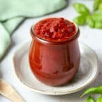 a jar filled with pizza sauce, on a table with herbs.