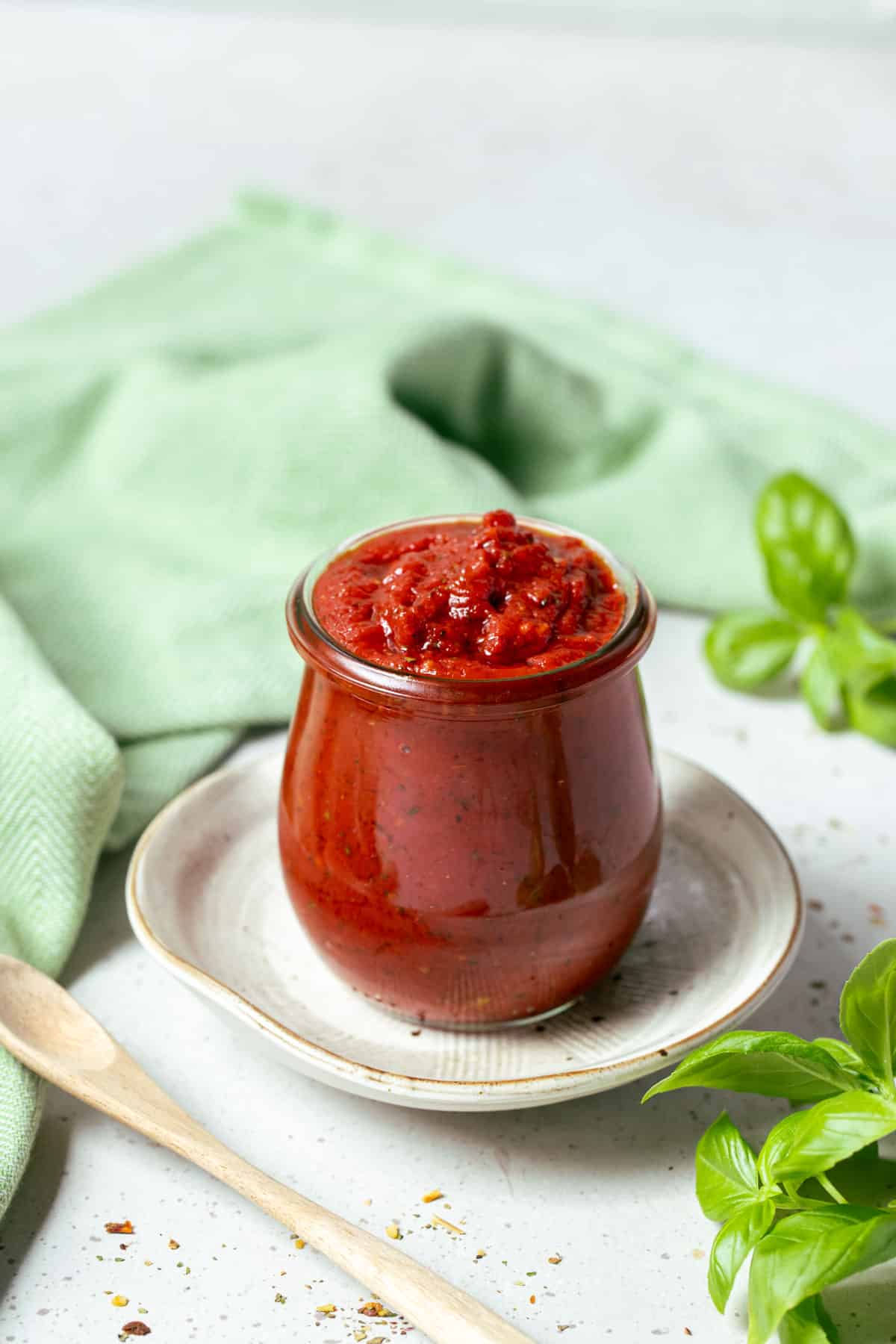 pizza sauce in a glass jar, on a table with basil leaves.