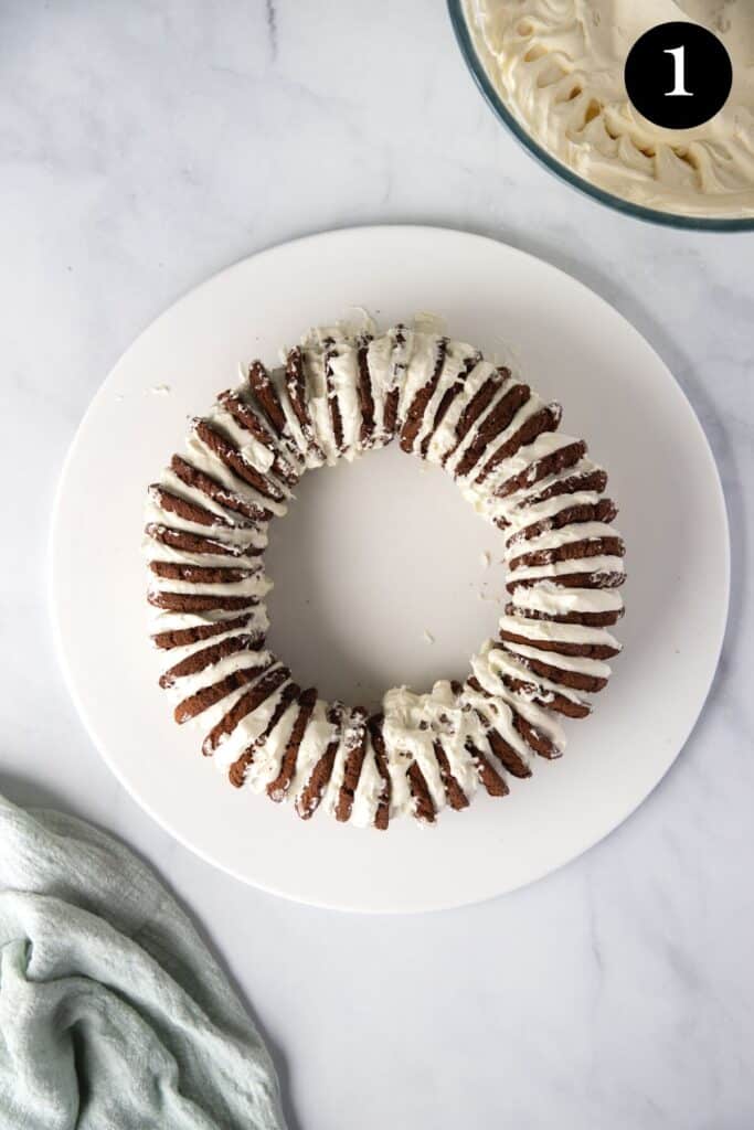 chocolate biscuits and cream layered into a wreath shape on a white plate.