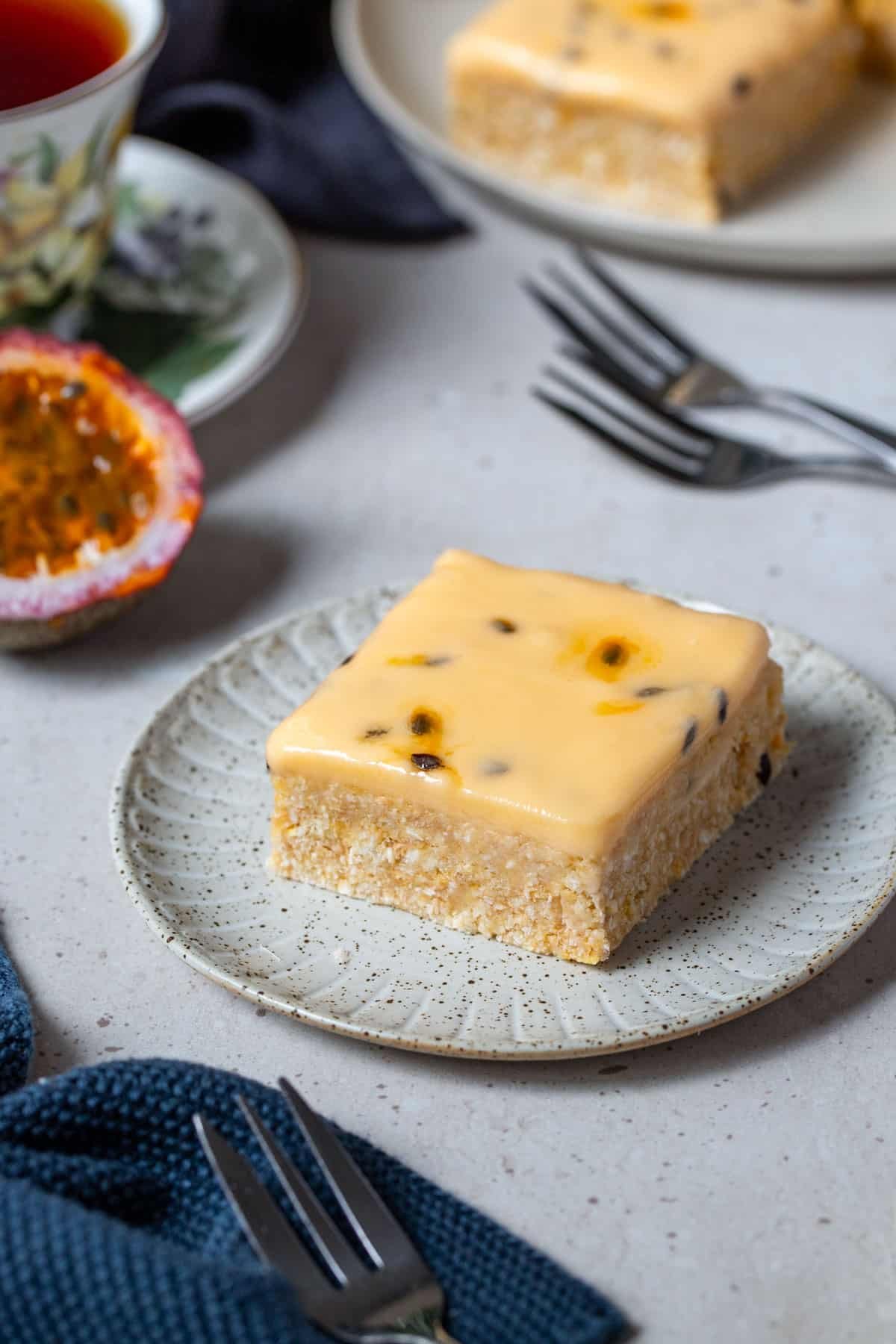 a piece of slice on a plate. It is topped with icing and passion fruit seeds.