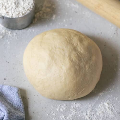 a ball of pizza dough on a table with flour and a rolling pin.