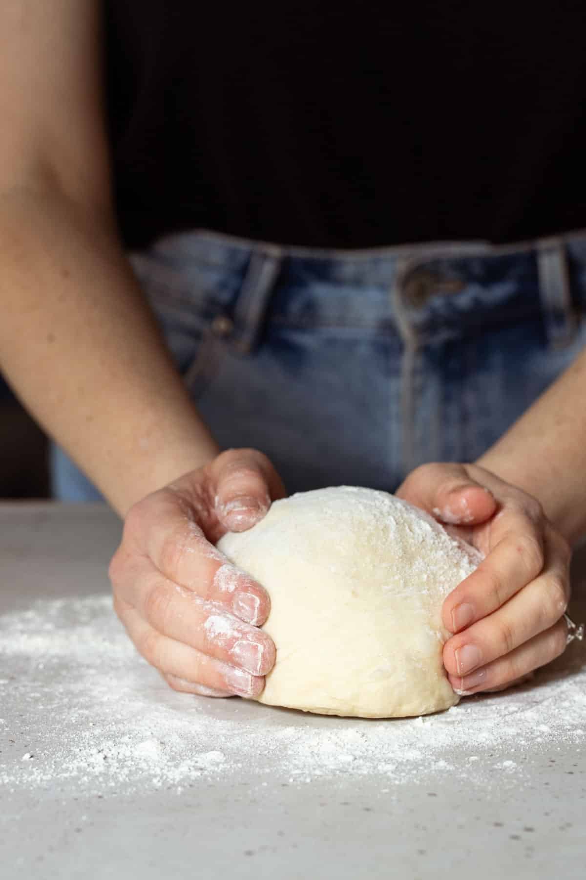 two hands shaping dough on a floured bench.