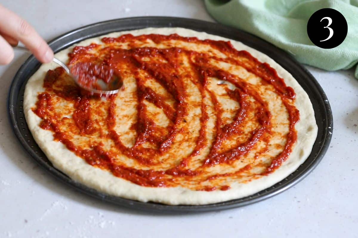 pizza sauce being spread over a pizza base.