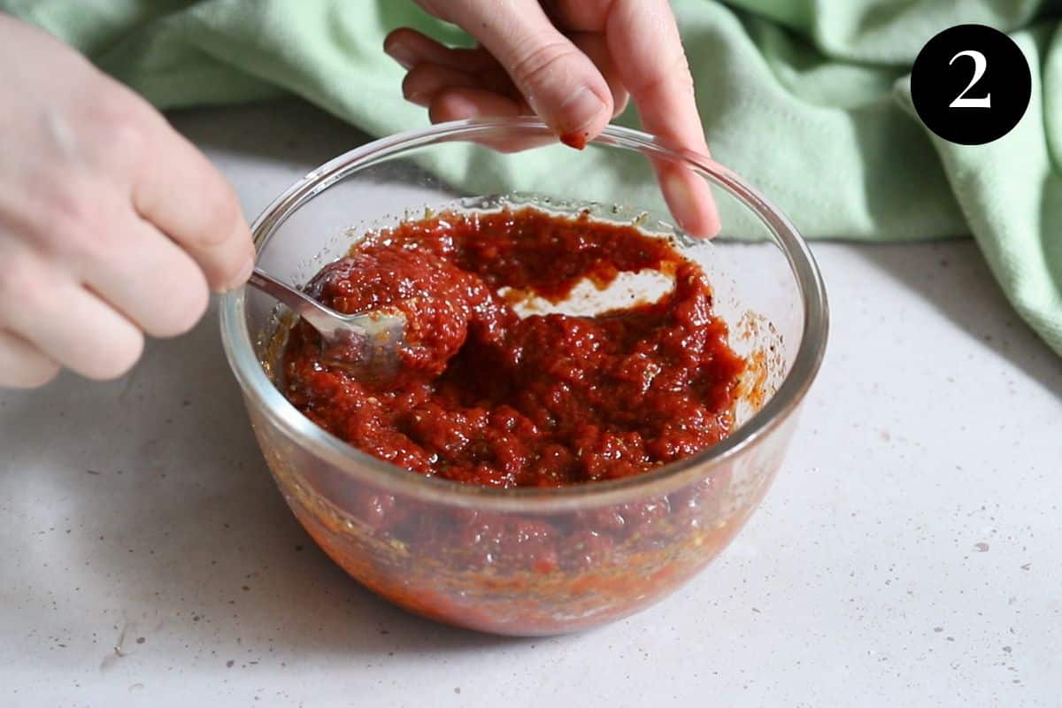 hands stirring pizza sauce in a bowl.