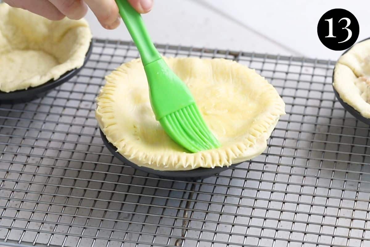 a pastry brush brushing egg over an uncooked pie in a tin.