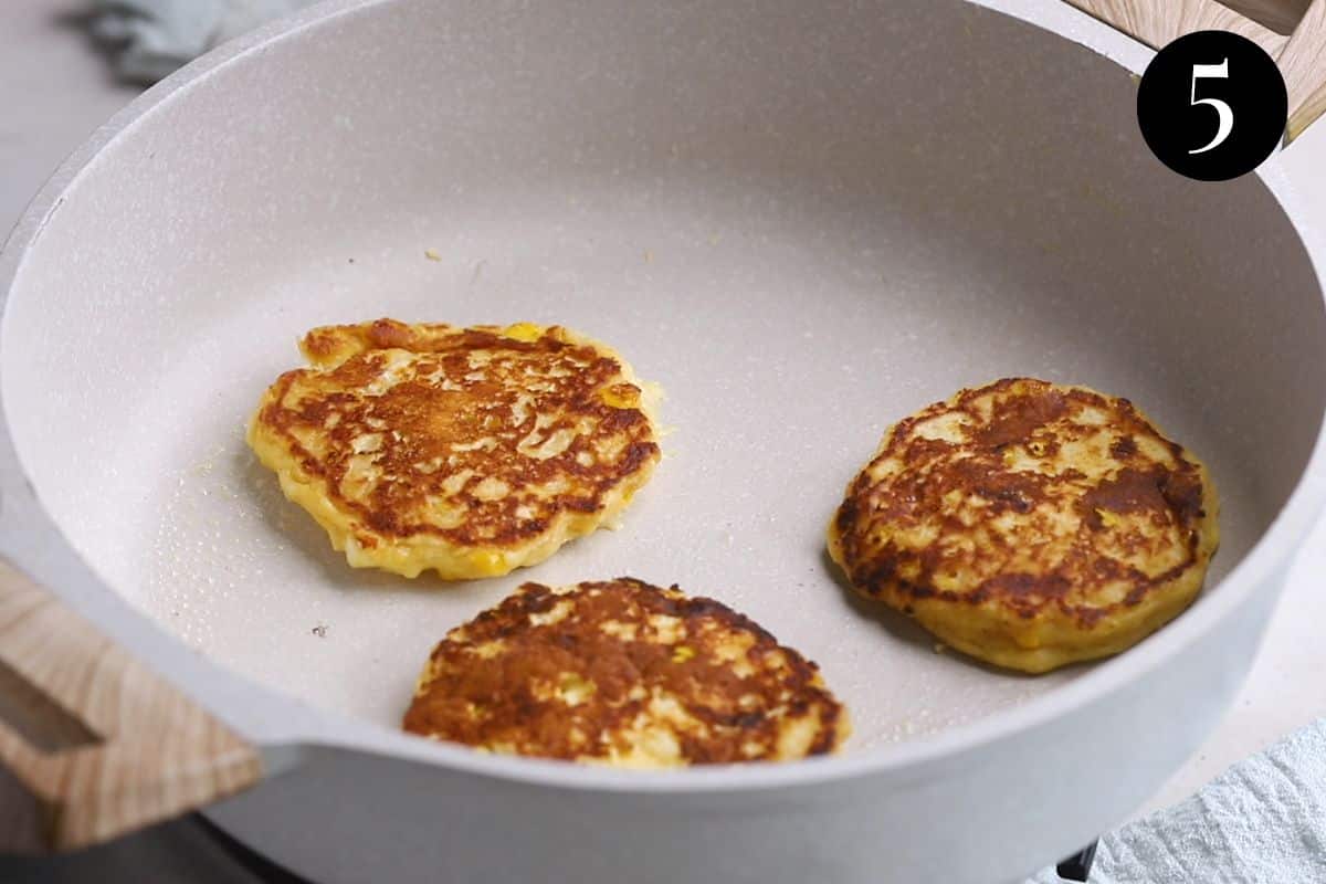 fritters in a pan after being flipped. Their tops are golden brown.