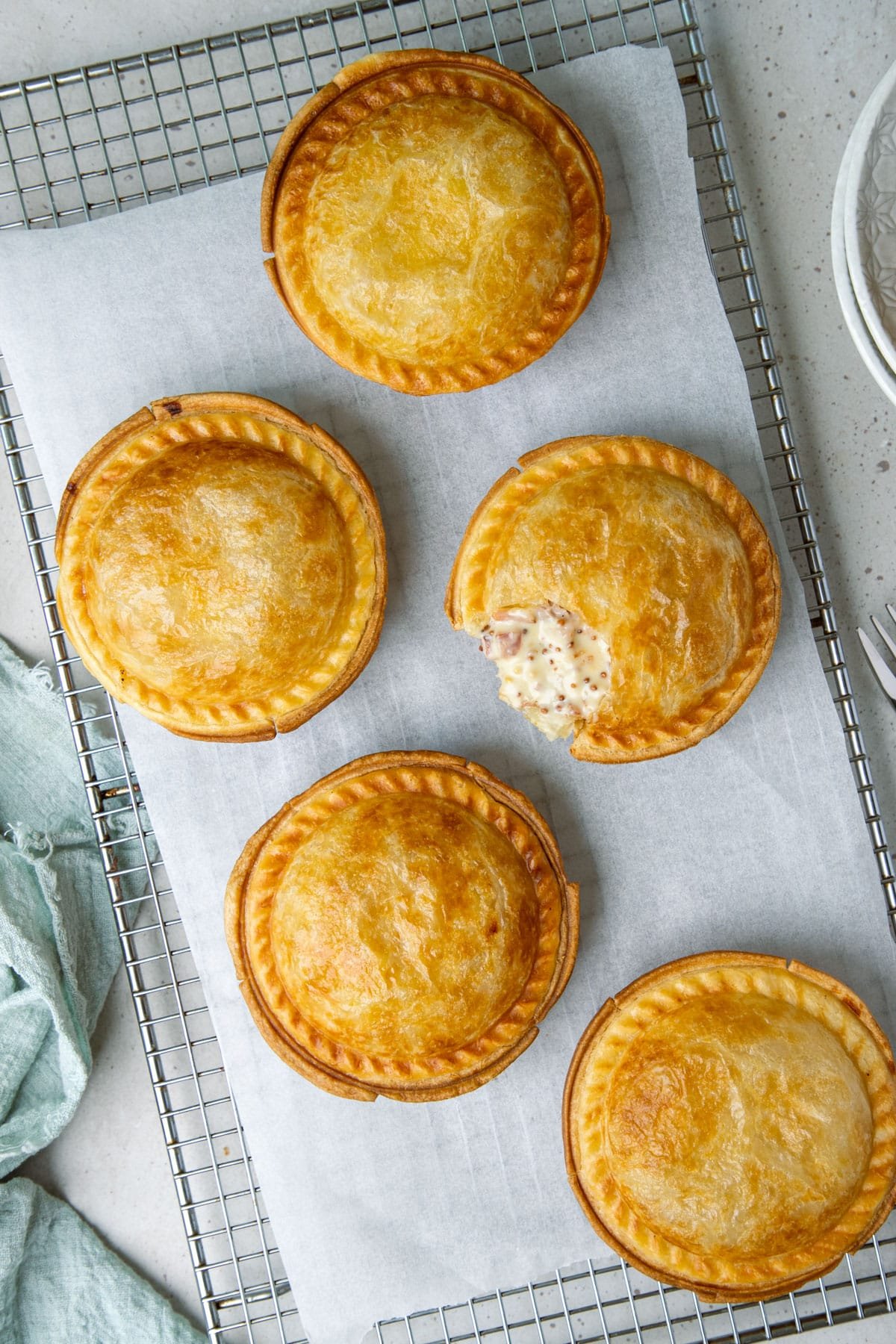 golden pies topped with puff pastry on a wire rack.