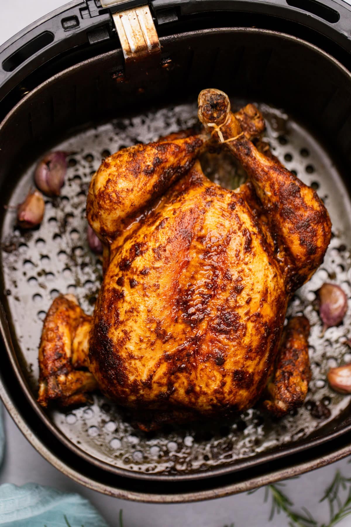 a whole, roasted chicken resting in an air fryer basket.