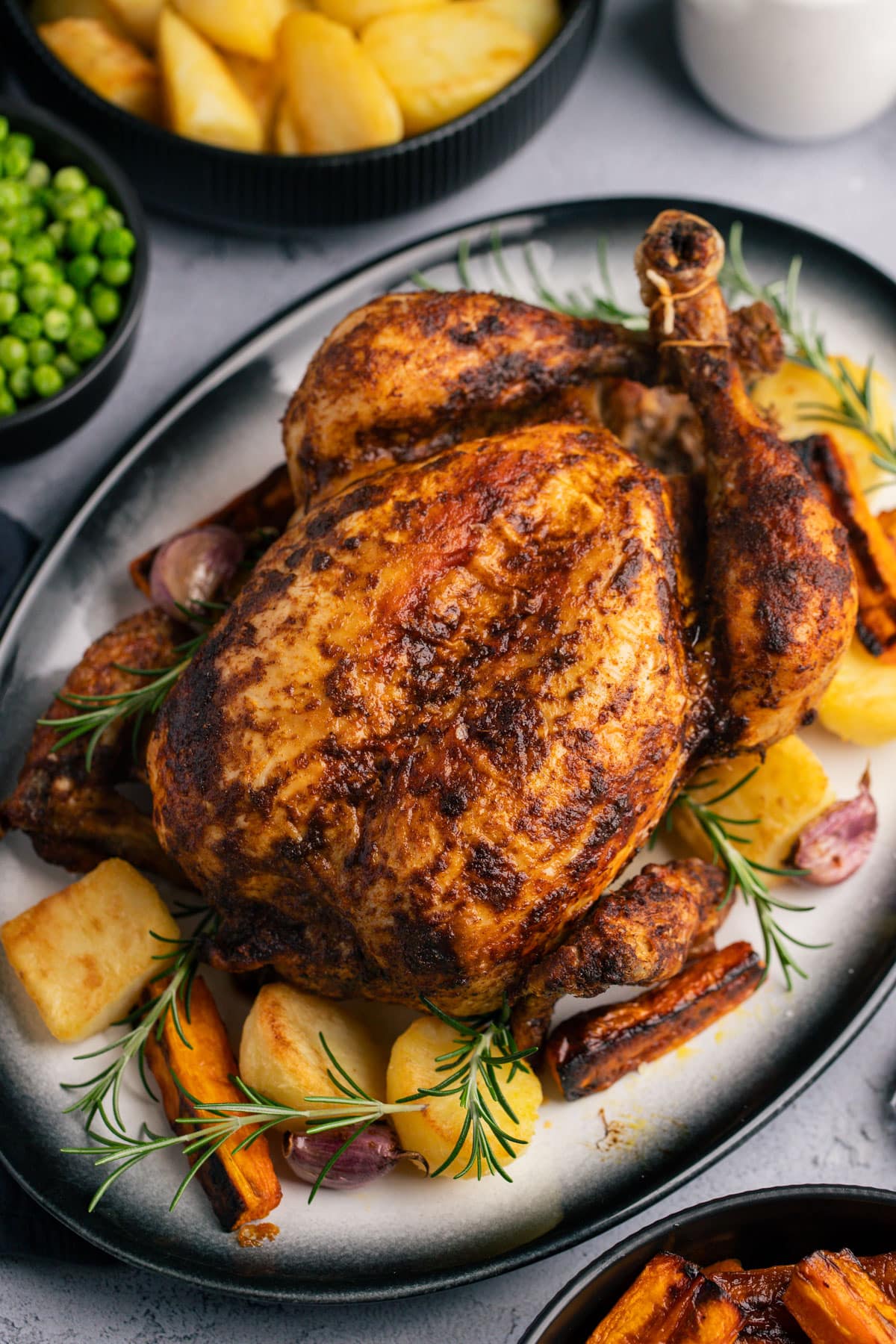 a whole roasted chicken on a plate with roasted vegetables and fresh rosemary.