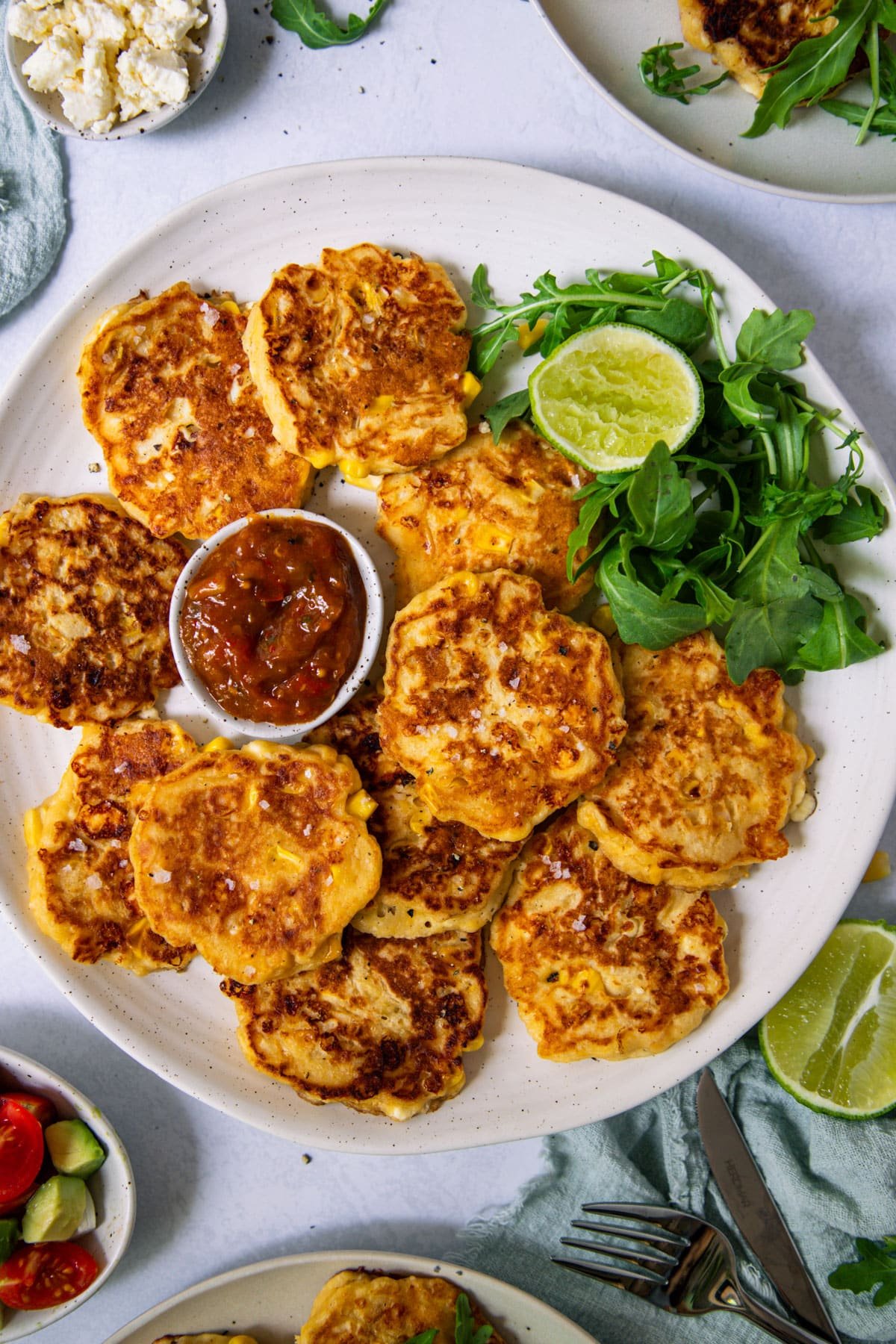 a plate of corn fritters with salad and sauce.