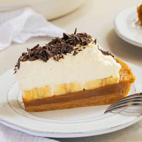 a slice of banoffee pie on a plate. It is topped with whipped cream.