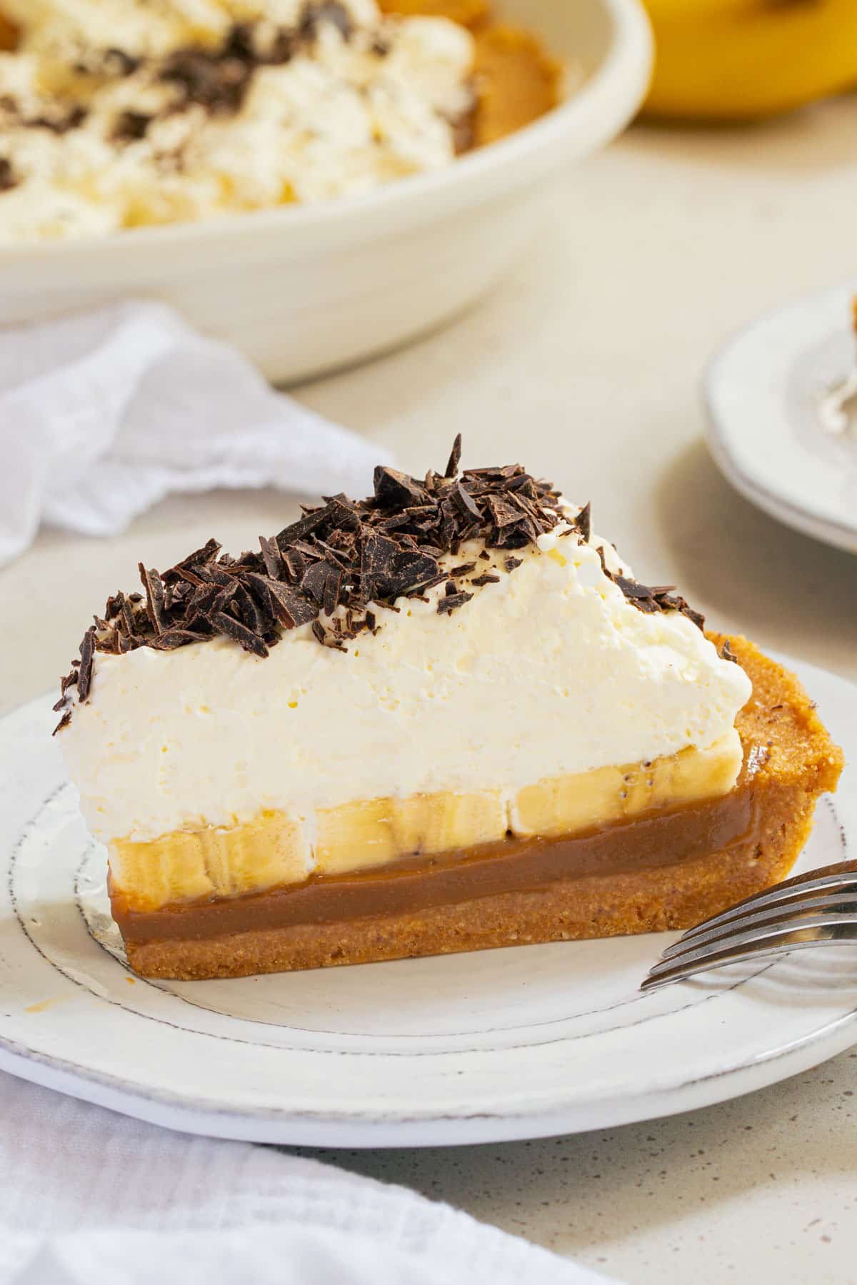 a slice of banoffee pie on a plate topped with whipped cream and chocolate.