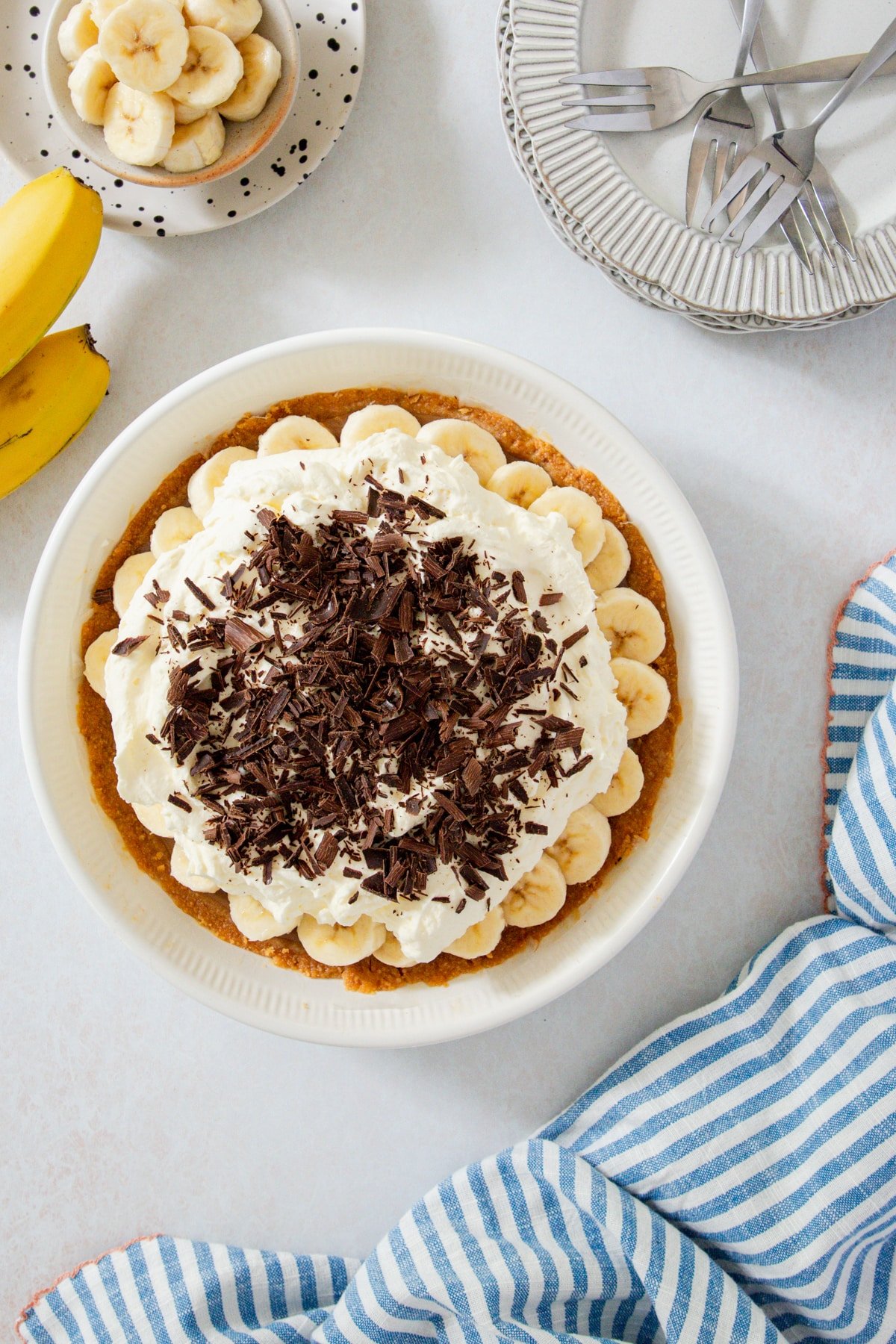 a whole banoffee pie on a table, with slices of banana and plates.