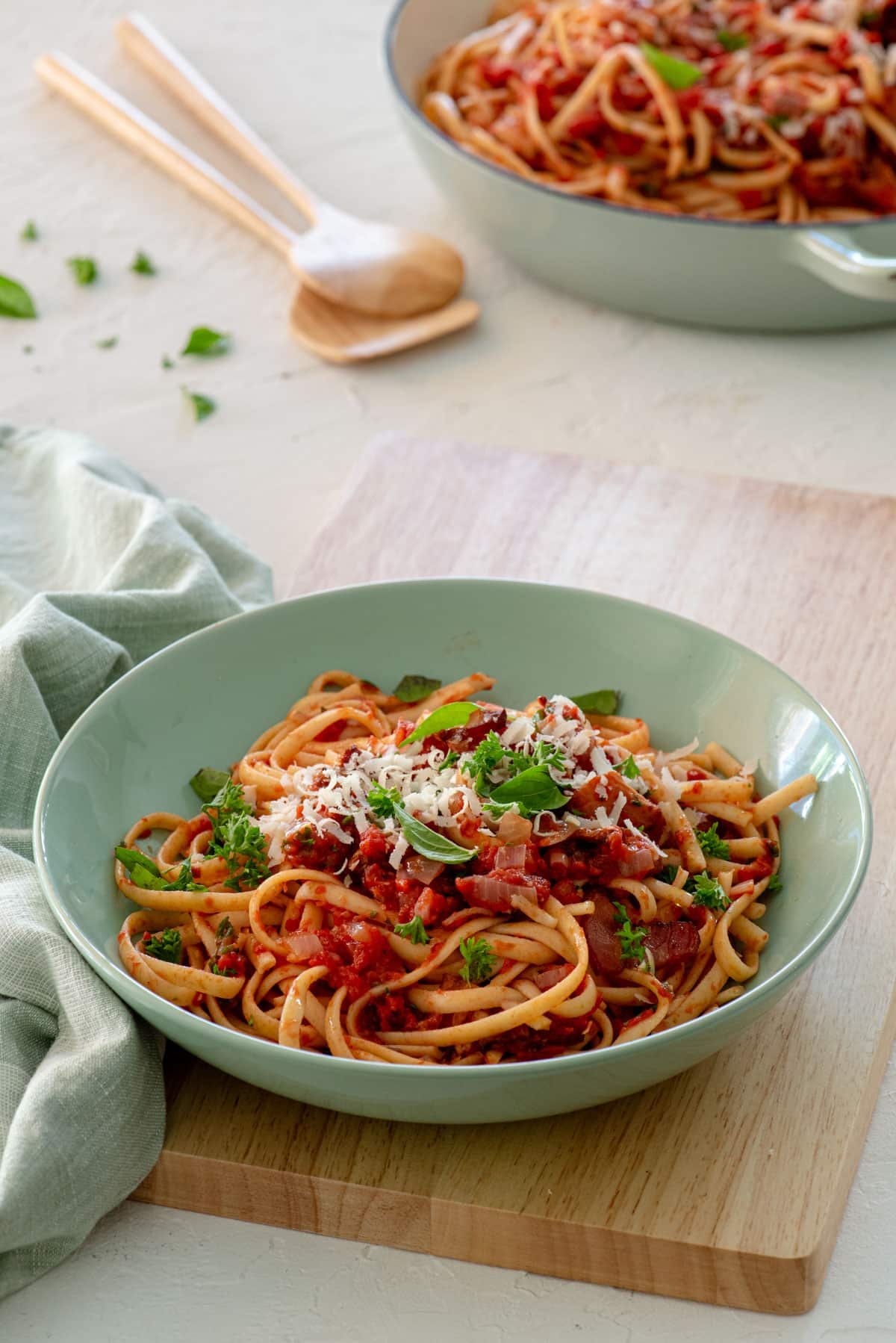 a bowl of pasta in tomato sauce topped with bacon and fresh herbs.