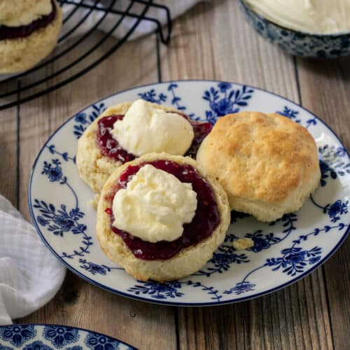a plate of scones, topped with jam and cream.