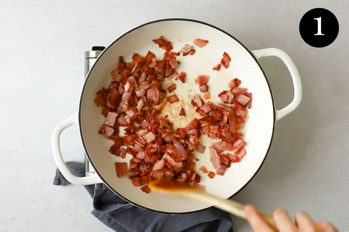 pieces of bacon frying in a pan with a wooden spoon.