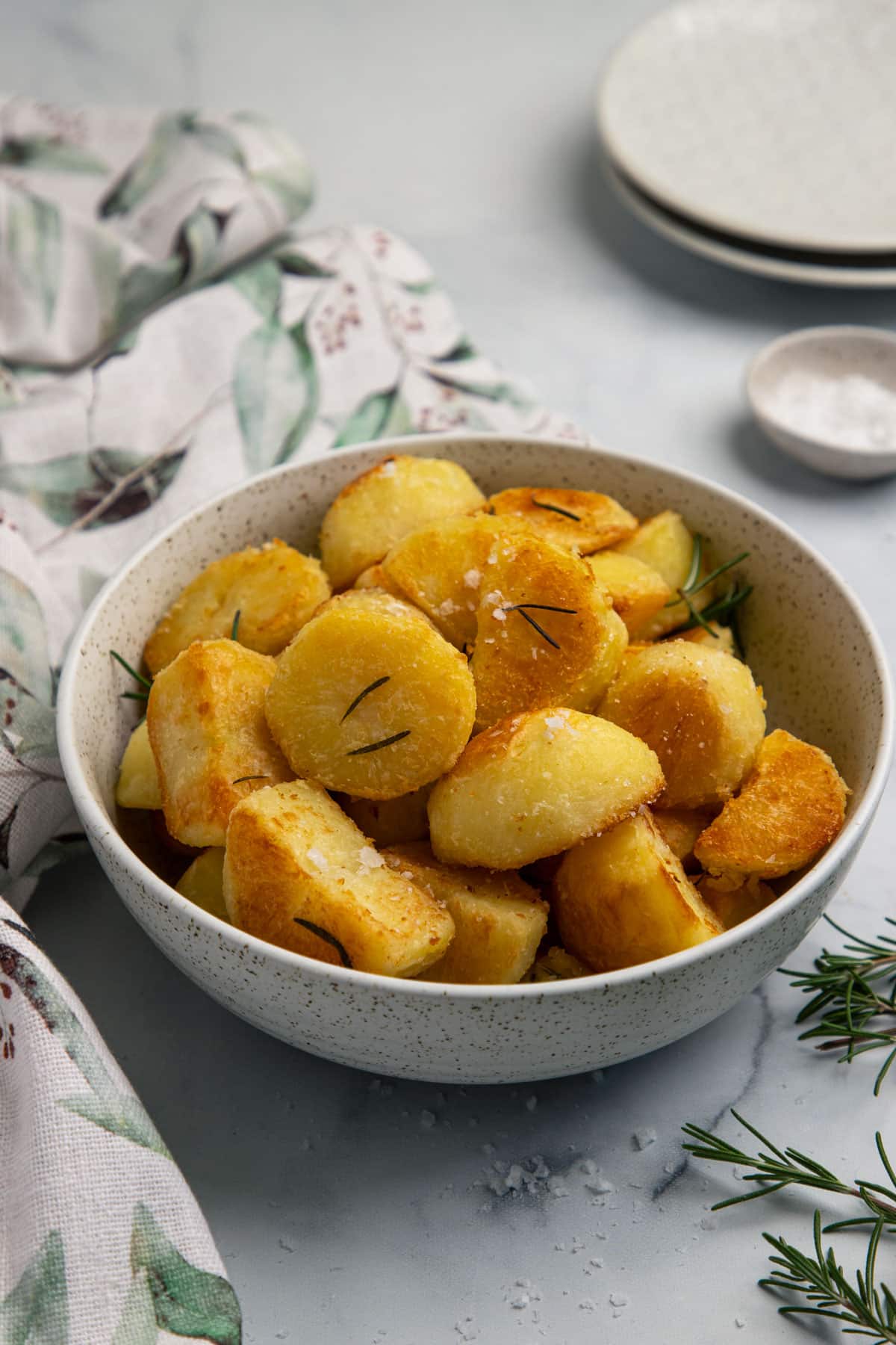 a bowl of roasted potatoes on a table with rosemary and salt.
