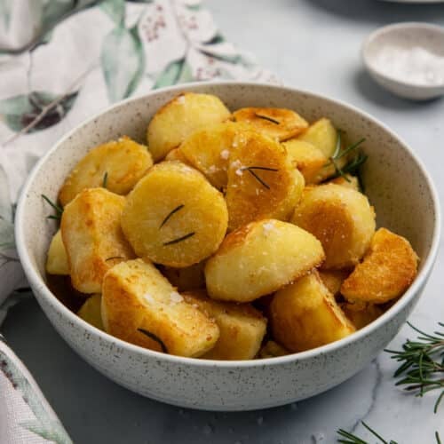 a bowl of roast potatoes, topped with rosemary and salt flakes.