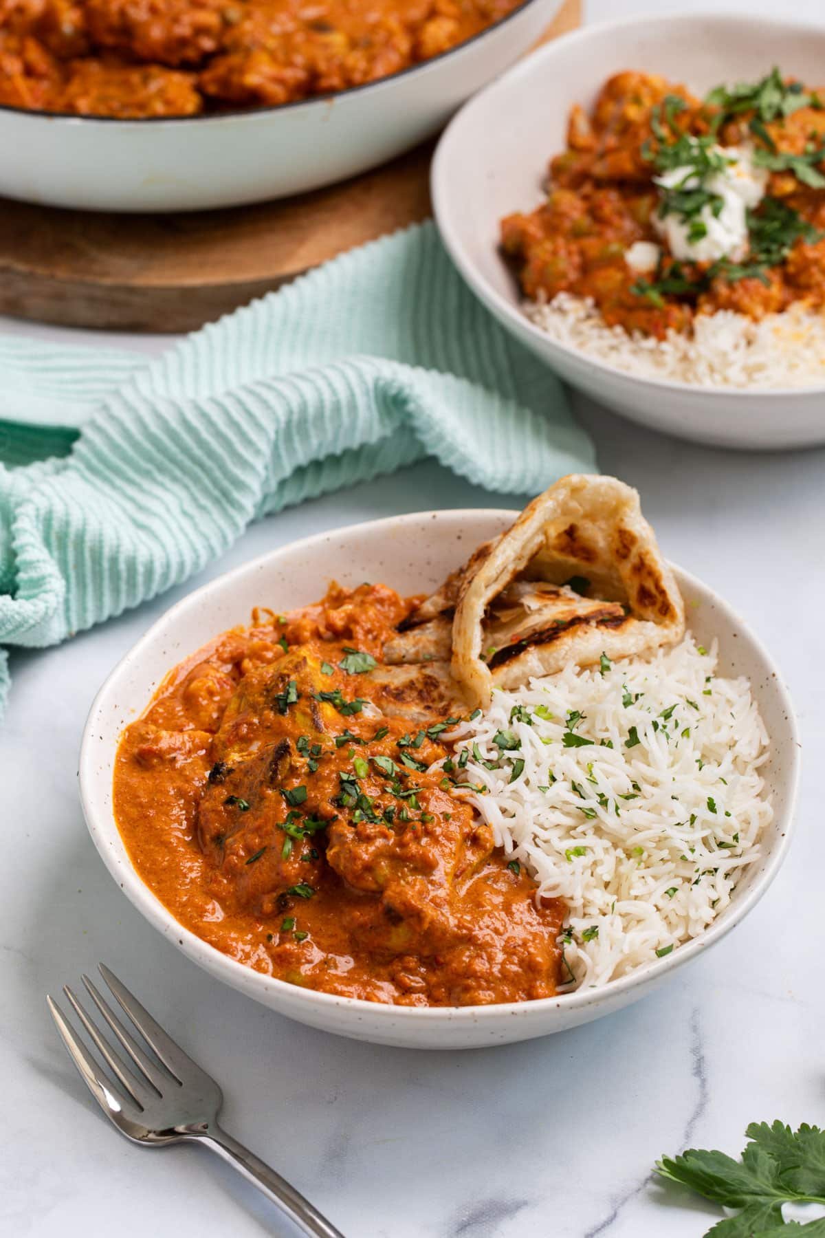 a bowl of tikka masala on a table, topped with naan bread and herbs.