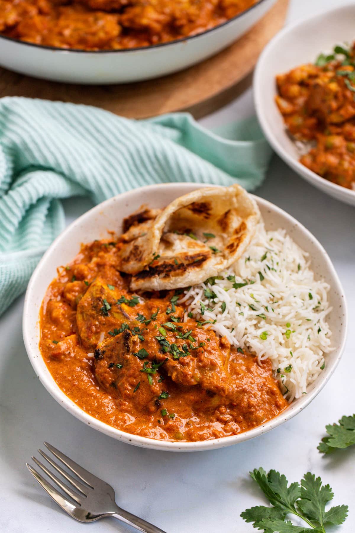 a bowl of tikka masala and rice on a table. There is naan bread tucked into the side.