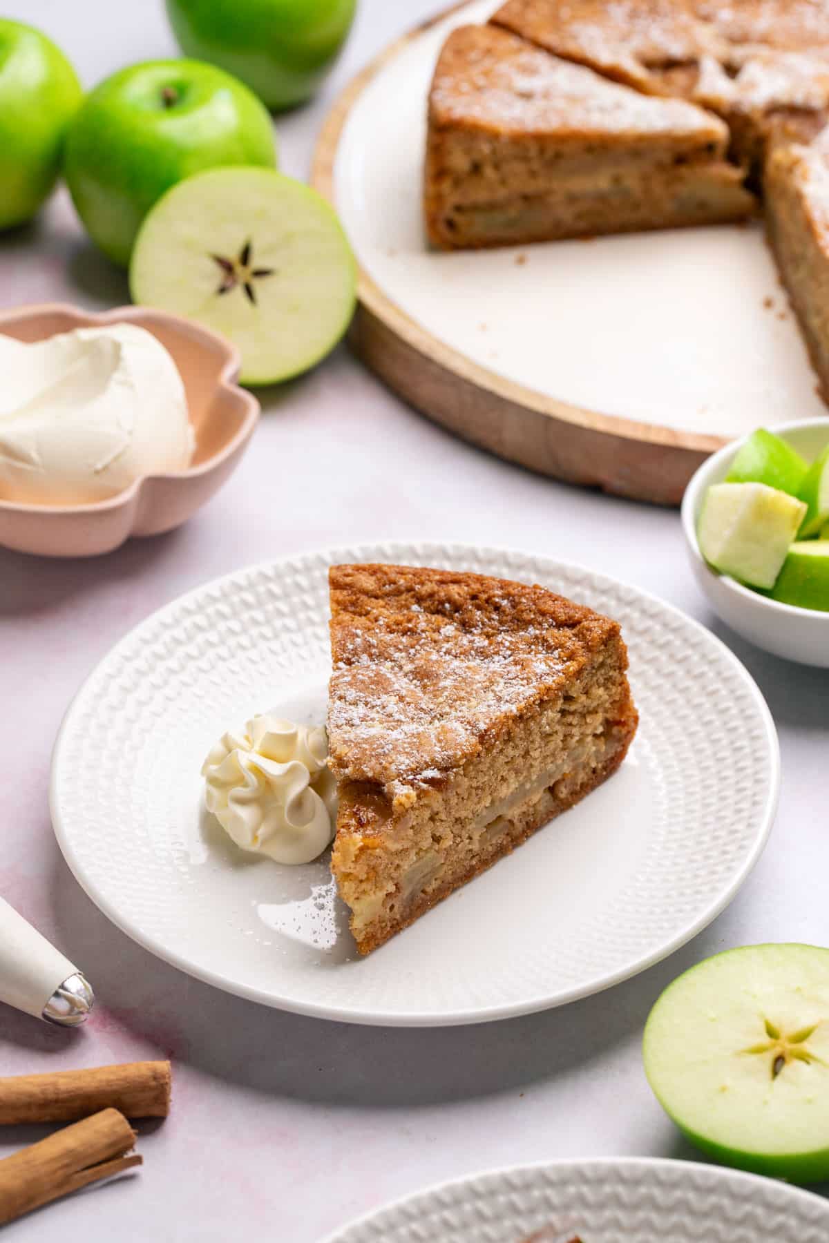 a slice of cake on a plate, with sliced apples and whipped cream.