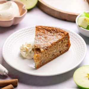 a slice of apple cake on a plate with whipped cream.