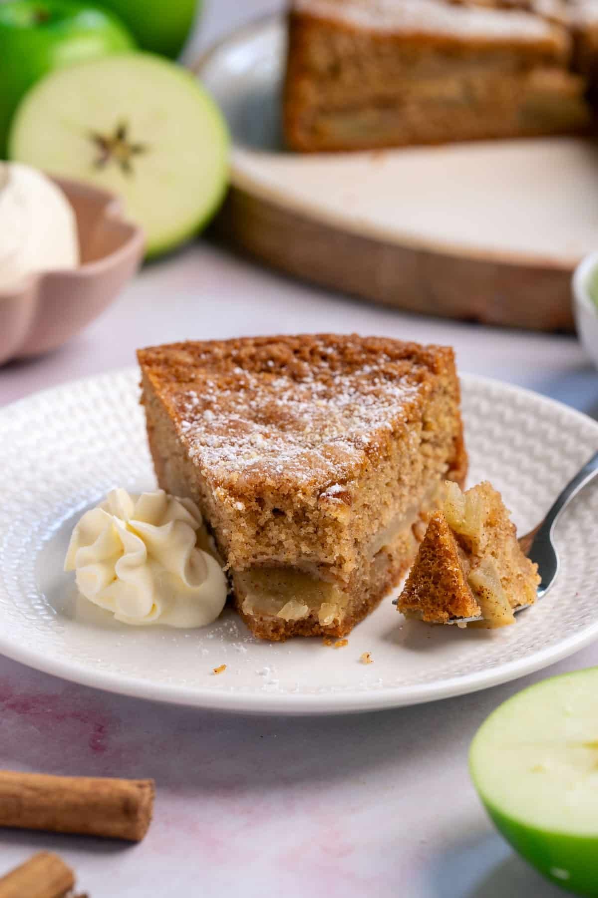 a piece of apple cake on a plate with cream and a fork.