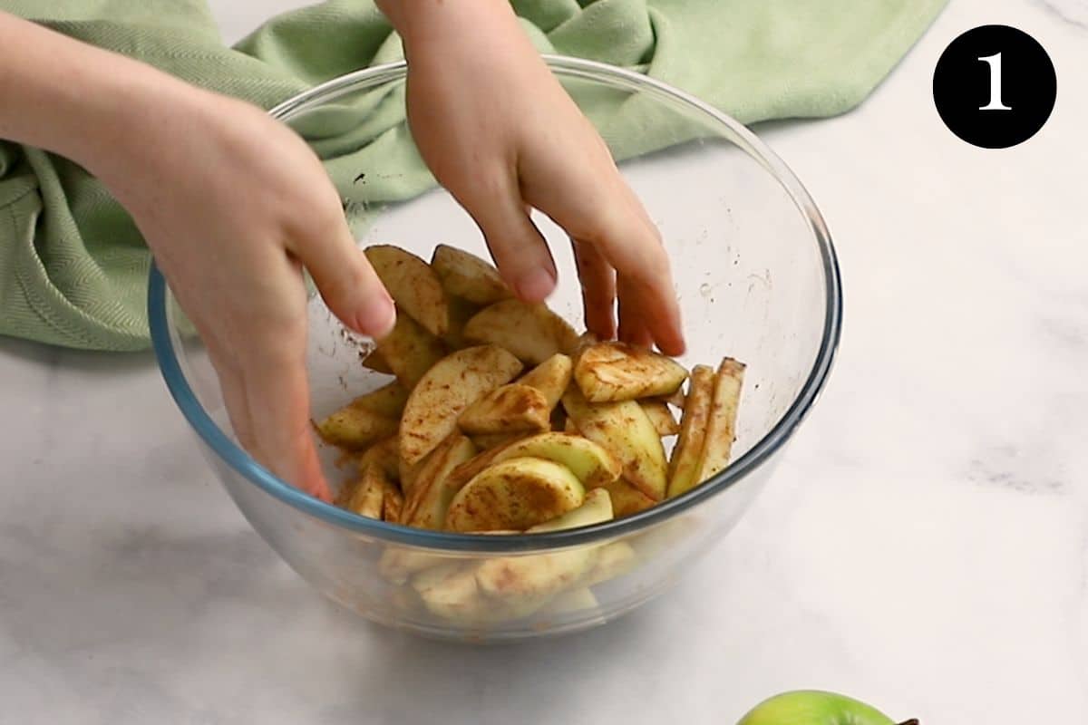 hands mixing sliced apples and cinnamon in a bowl.