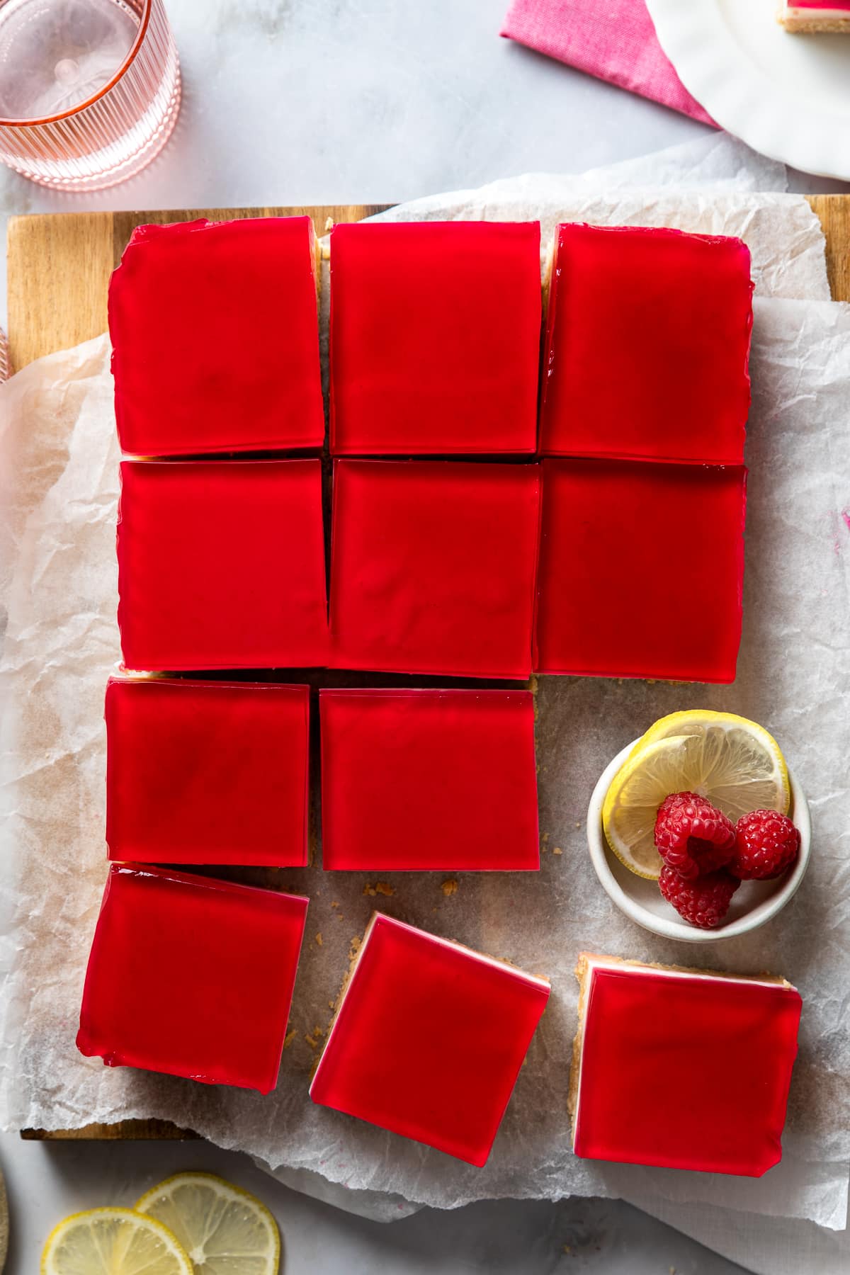 top view of a jelly slice, cut into pieces on a board with lemon and berries.